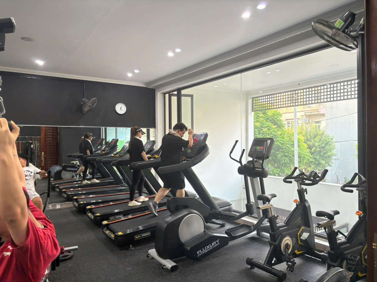 Khu cardio ngoài trời tầng 1 với dãy máy chạy bộ, xe đạp tập và máy elliptical bên cửa kính lớn